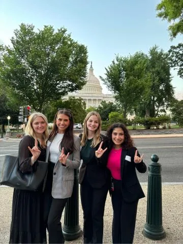 4 students in front of US Capitol giving Hook 'Em hand sign