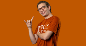 Portrait of Will Barrett wearing an orange LBJ t-shirt and giving the hook 'em hand gesture