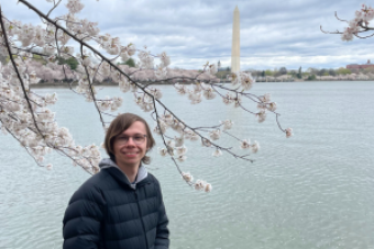 Photo of Matthew Willis next to cherry blossoms with the Washington Monument in the background